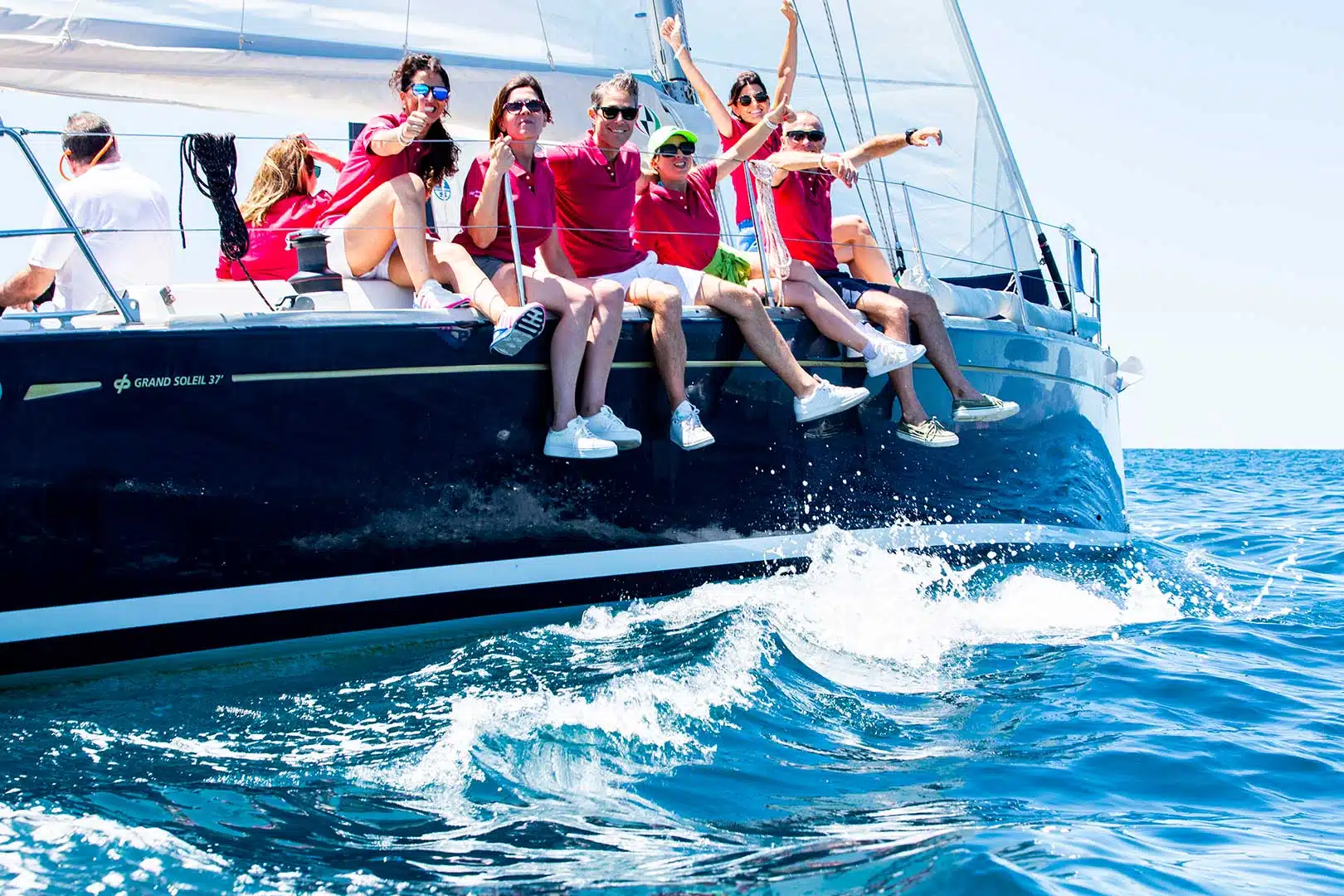 barca a vela per aziende – equipaggio in maglie rosse festeggia sulla prua di una barca a vela