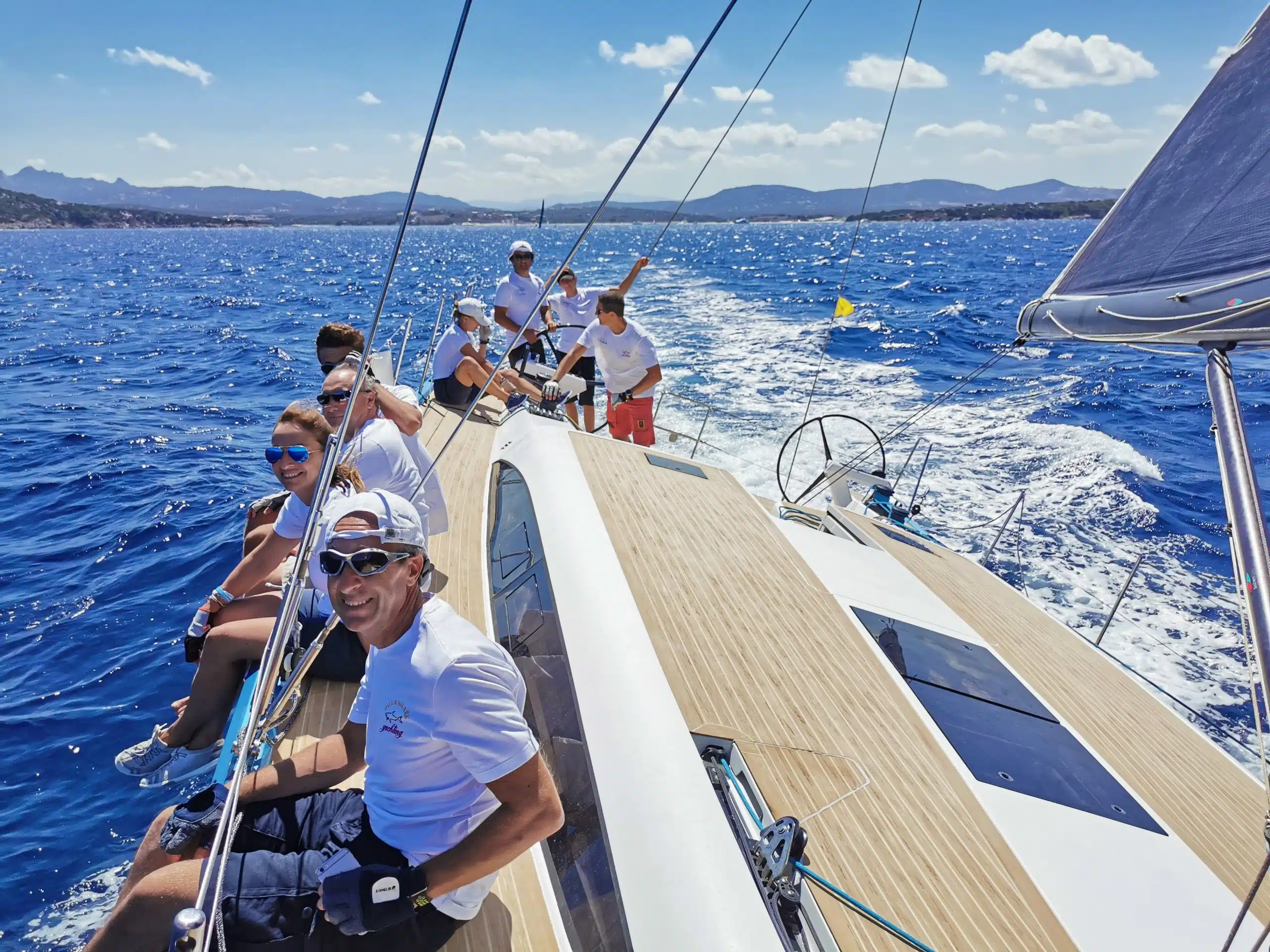 barca a vela per aziende – equipaggio su uno yacht in navigazione con la scia e la costa sullo sfondo